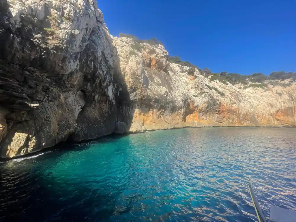 Dark limestone cave entrance in turquoise water cove