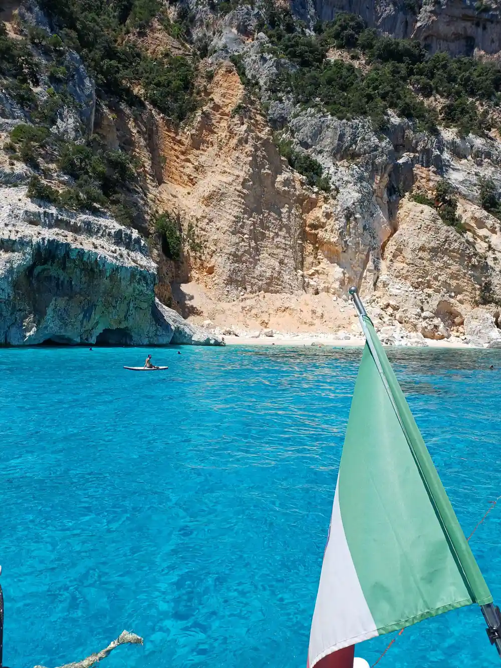 Italian flag on boat with rocky cliff and swimmers