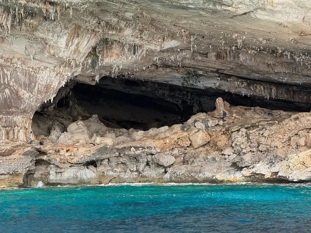 Large dark cave opening in limestone cliff above beach