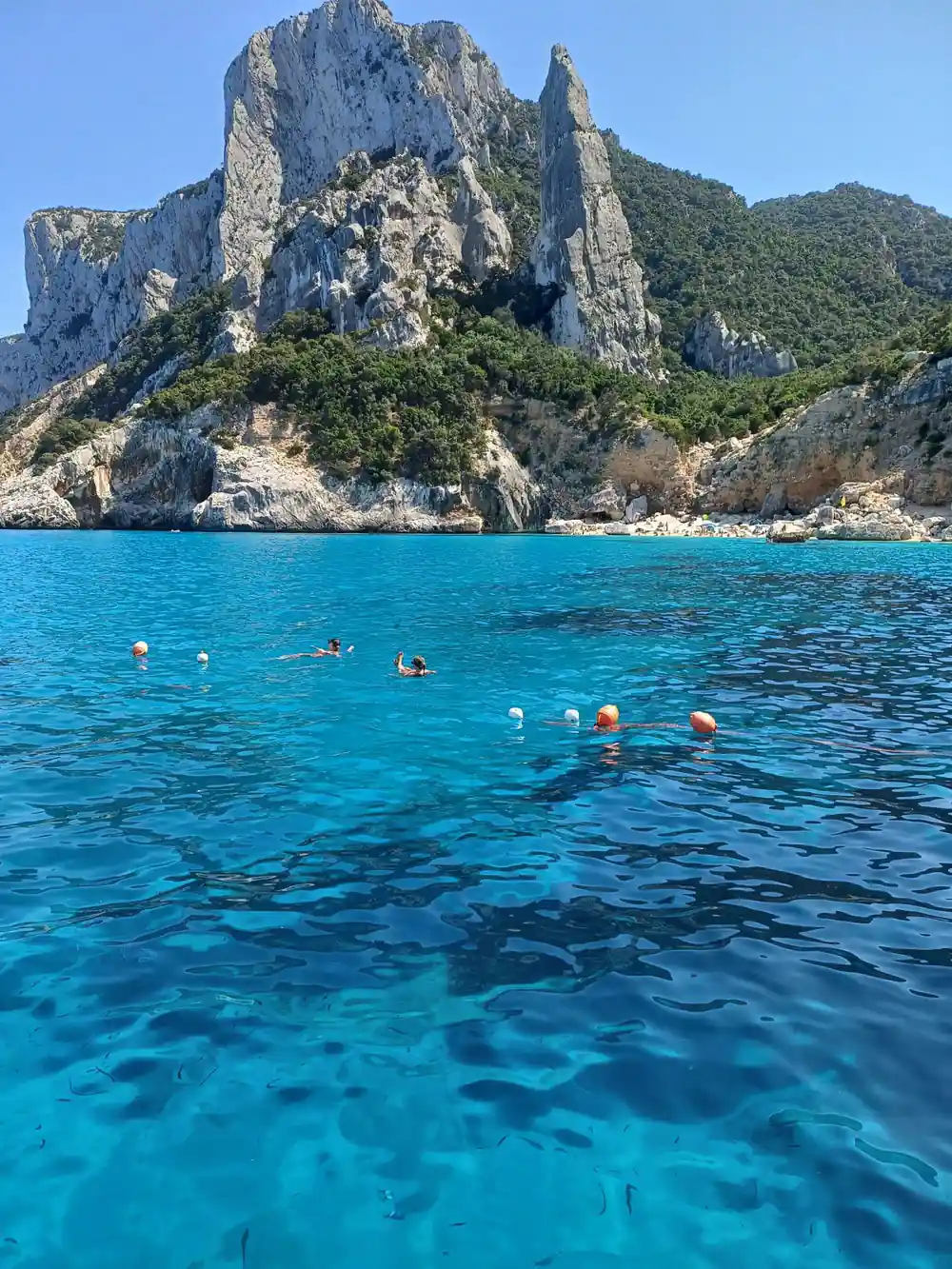 Multiple swimmers in clear turquoise water near rock formations