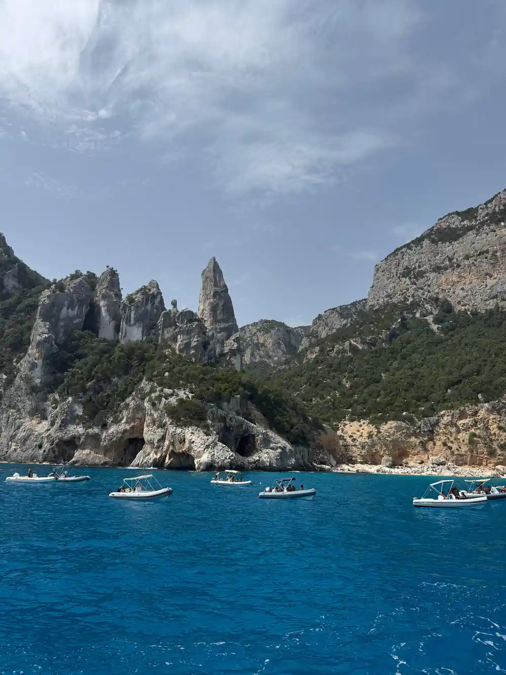 Multiple white boats anchored in turquoise cove near cliffs