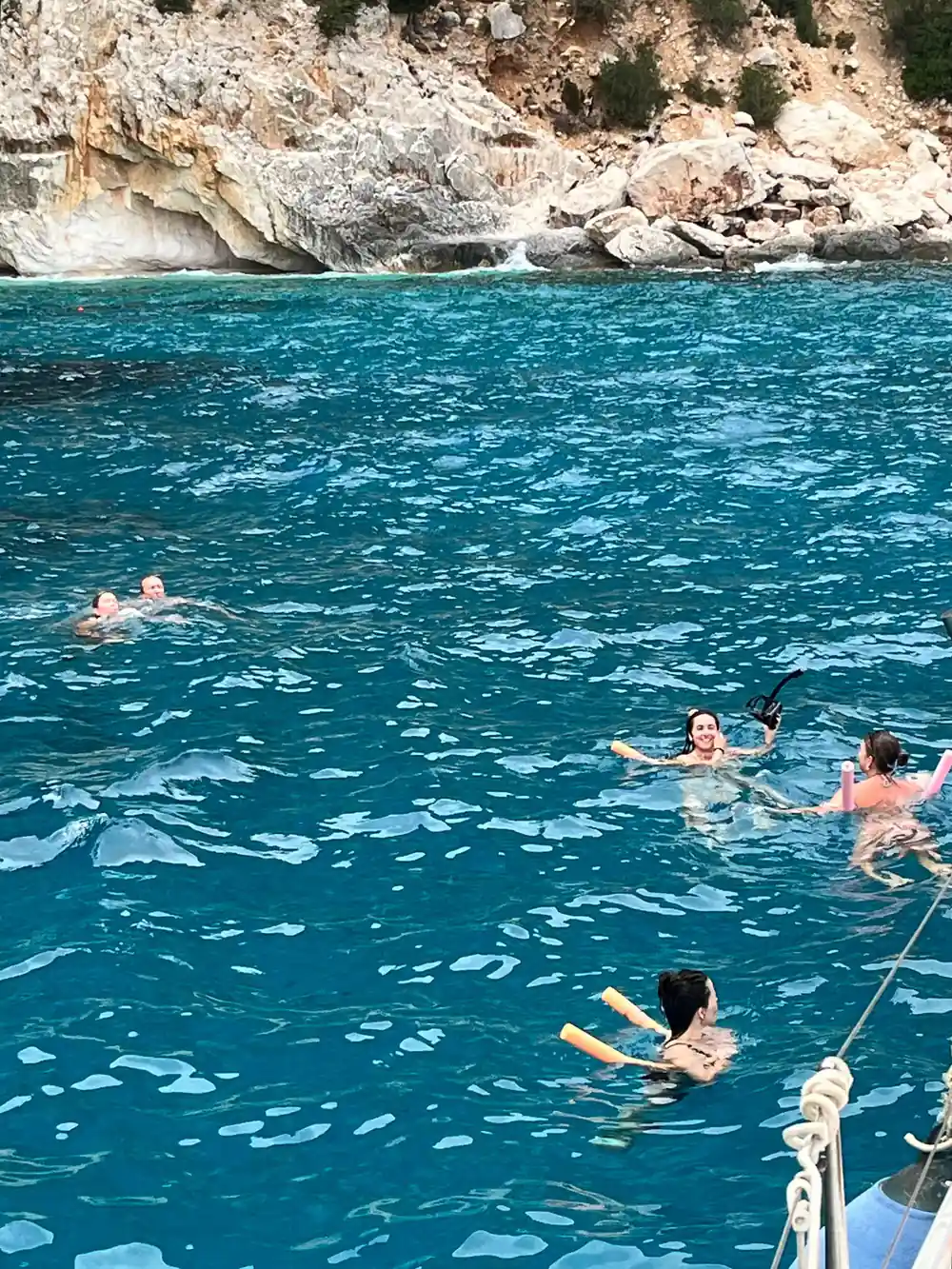 People swimming in turquoise water below white limestone cliff