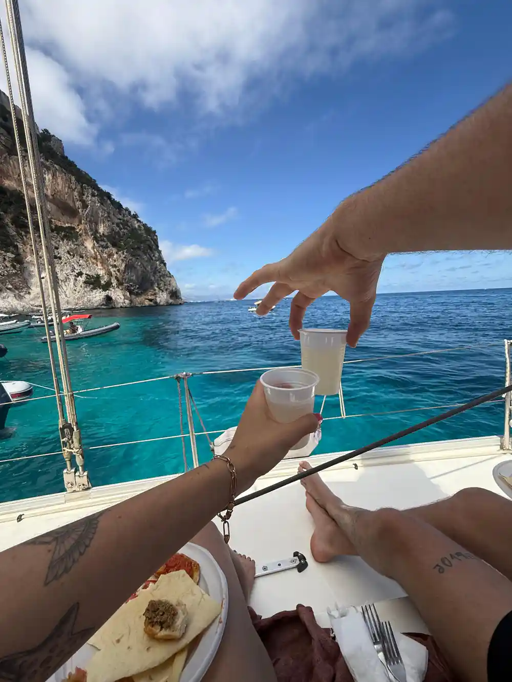 Person's hand pouring wine on boat with coastal cliffs behind