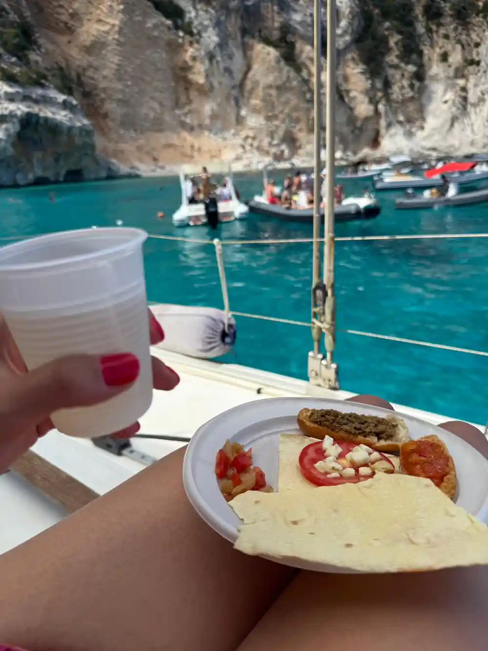 Plate of food on boat with wine glass and cliff view beyond