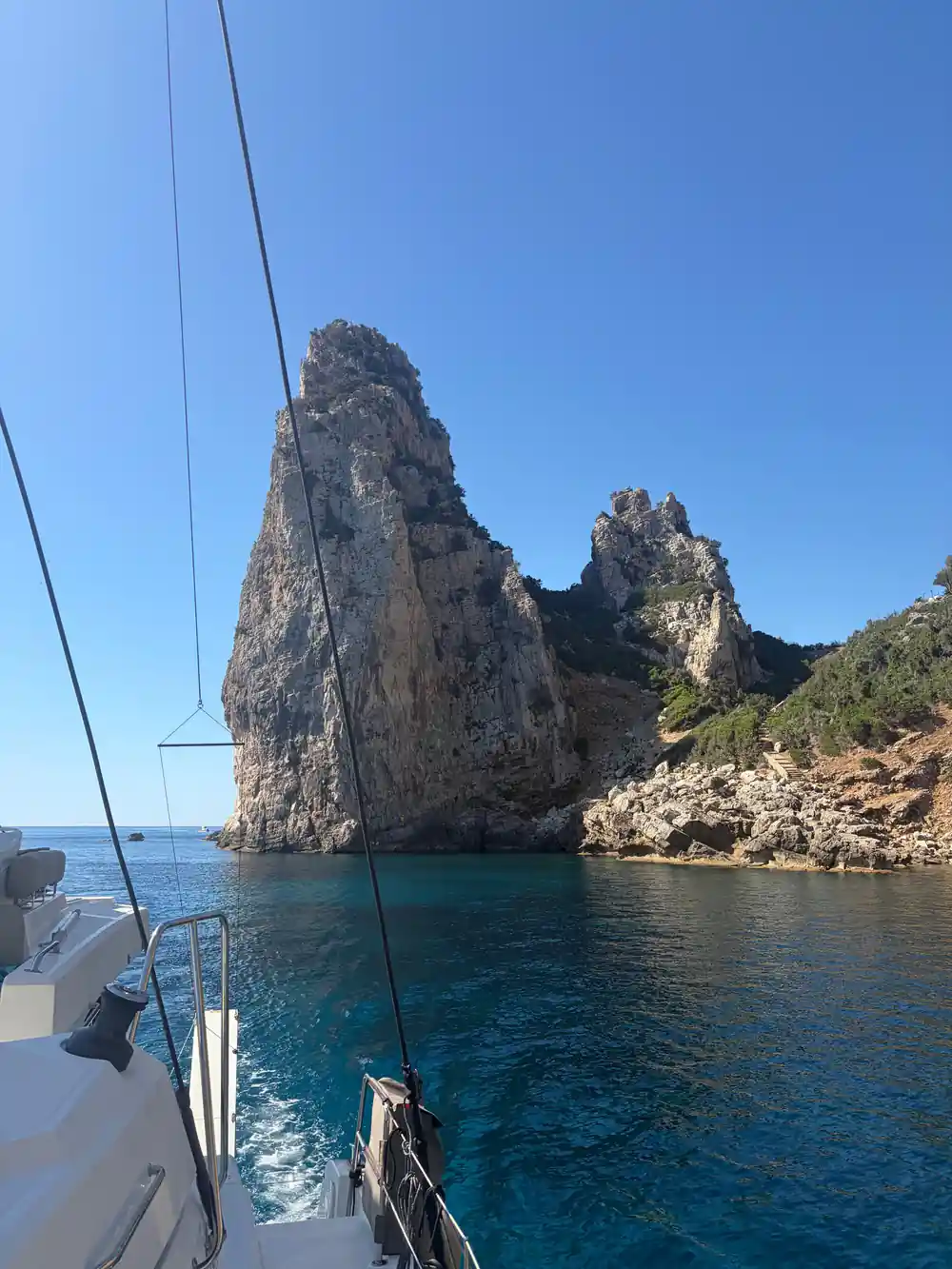 Sailboat approaching tall rocky sea cliff formation