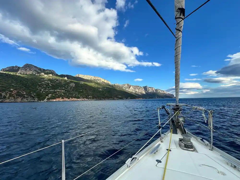 Sailboat bow sailing toward mountainous rocky coastline