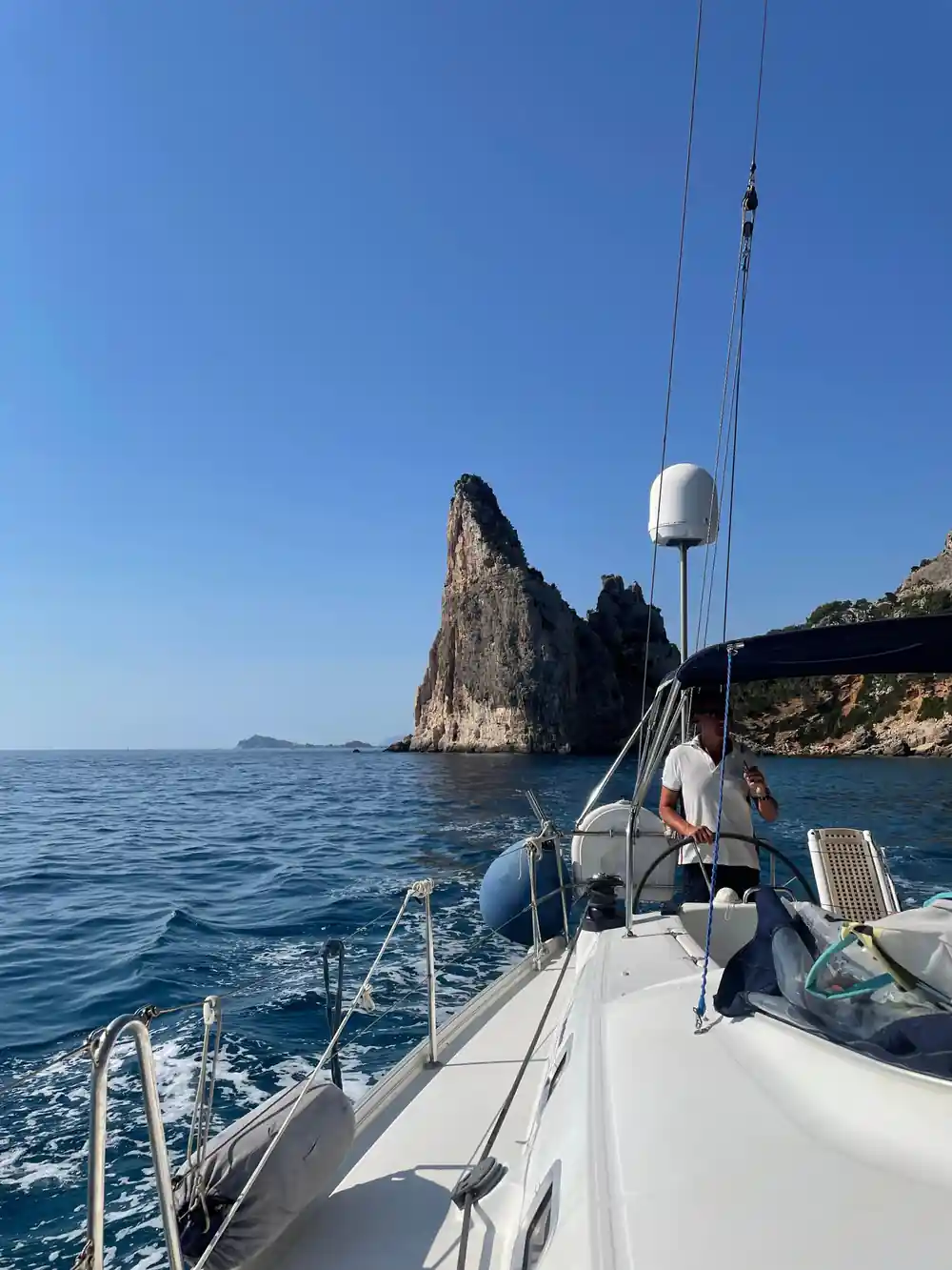 Sailboat sailing toward rocky peak in turquoise water