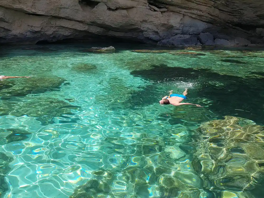 Snorkeler swimming in crystal clear turquoise water near cave