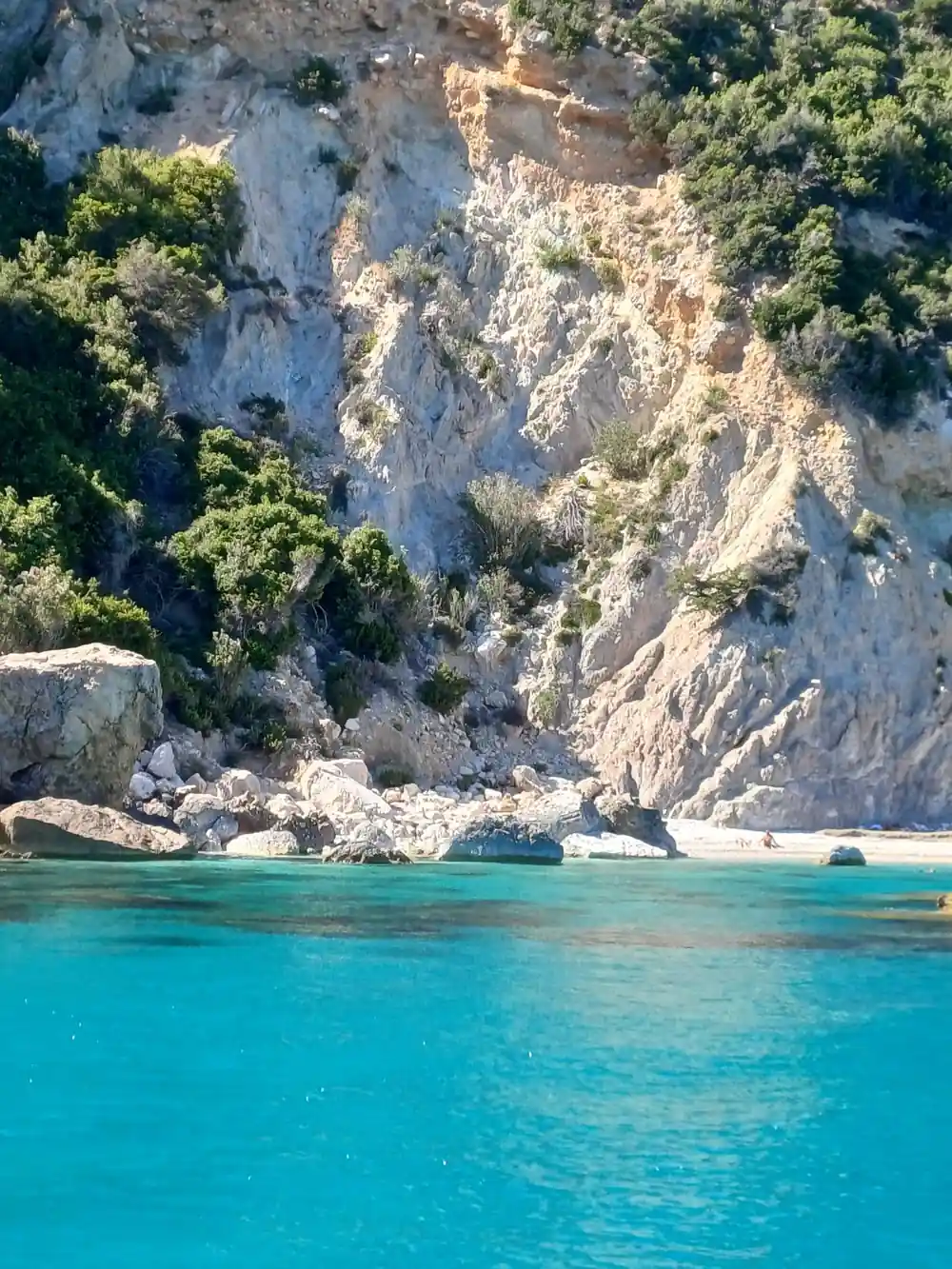Steep limestone cliff face above white beach and water
