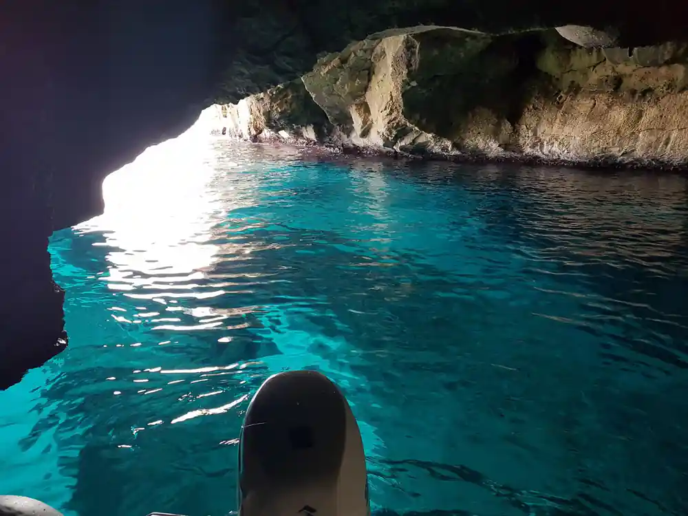 Sunlit cave opening in sea cliff with turquoise water