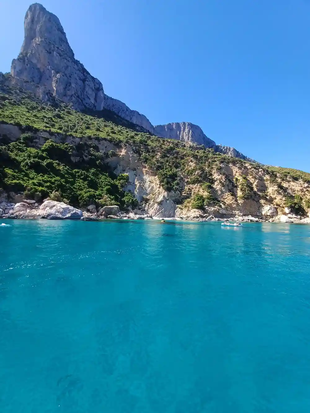 Tall rocky peak above turquoise water with boats