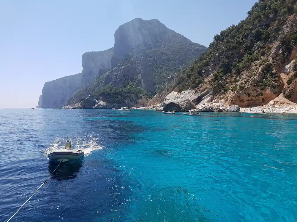 Turquoise bay with moored boat and steep mountain coastline