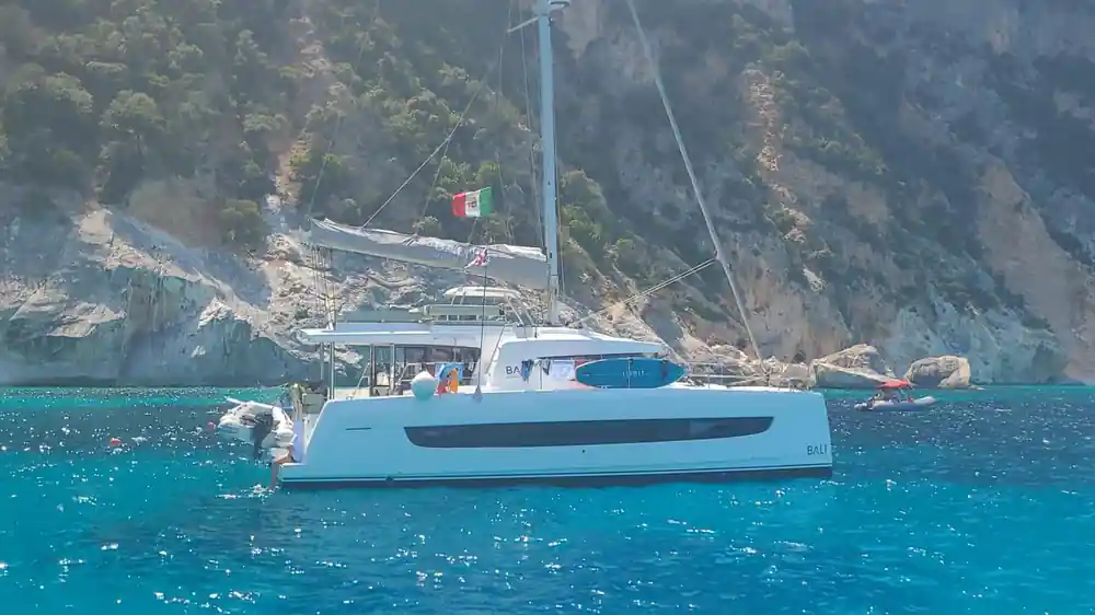 White catamaran at anchor below tall dramatic sea cliffs