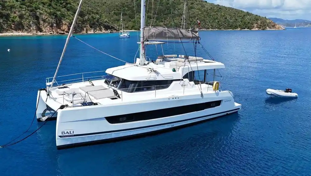 White catamaran anchored in sheltered blue bay with green hillside